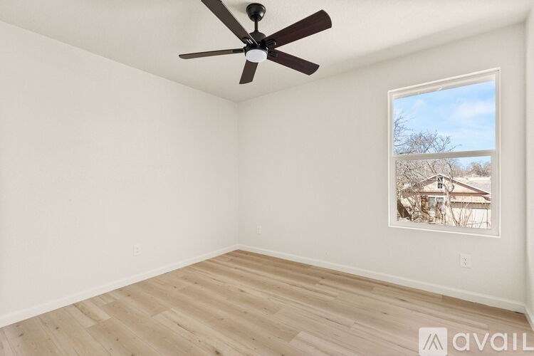 A room with a ceiling fan and a window showing a view of a house.