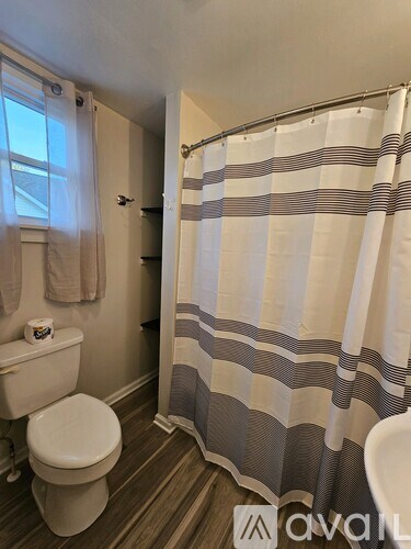 A bathroom with a toilet, a shower curtain, and a towel hanging on the wall.