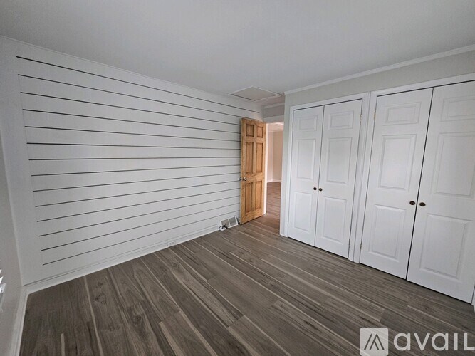 A room with wooden flooring and white walls with a doorway leading to another room.
