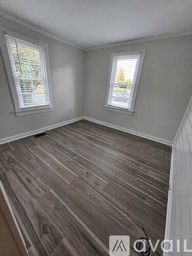 A room with wooden flooring and two windows.