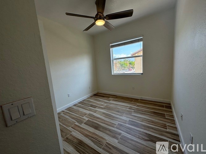 A room with a ceiling fan and a window showing a view of a street.