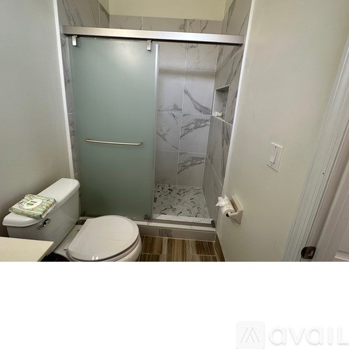A bathroom with a toilet, a shower with a glass door, and a marble floor.