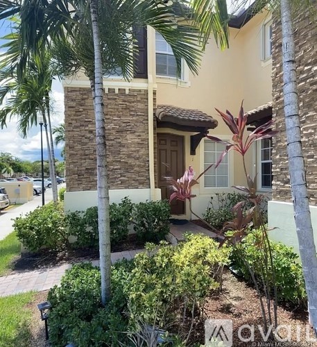 A house with a brown door and windows surrounded by green plants.