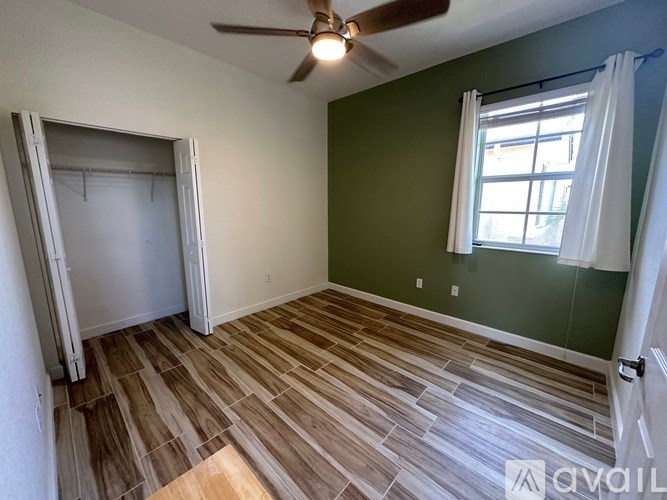 A room with a ceiling fan and a window with white curtains.