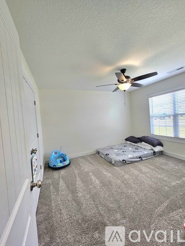 A room with a bed, a toy car, and a fan.