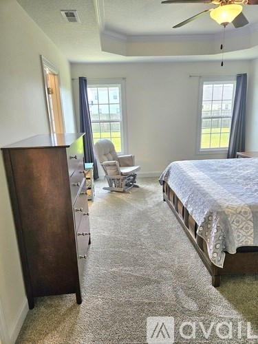 A bedroom with a bed, chair, and a fan.