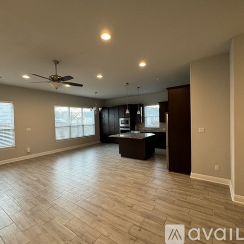 A spacious room with a ceiling fan and a kitchen area with a counter and cabinets.