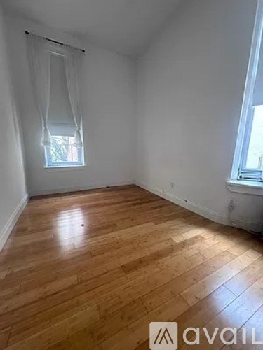 A room with wooden flooring and a window with white curtains.
