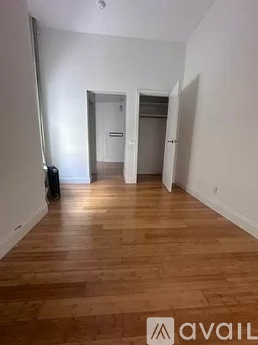 A room with wooden floors and white walls, with a door in the background.