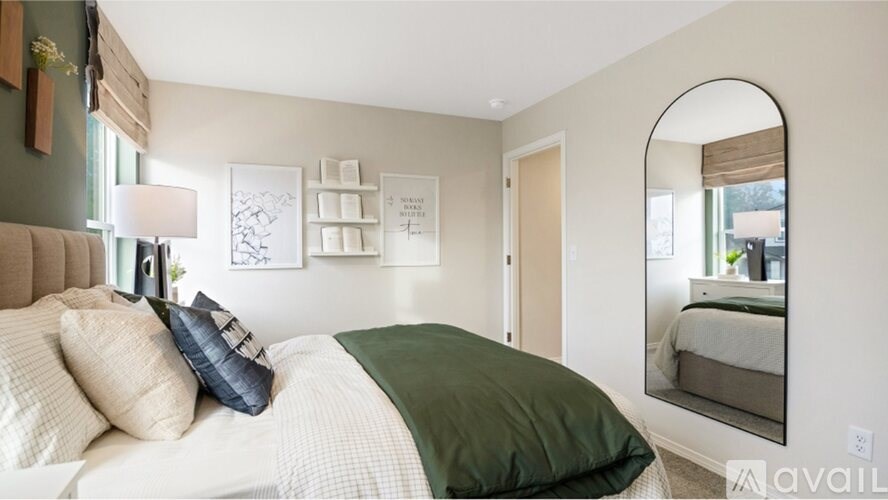 A bedroom with a bed, pillows, a lamp, and a mirror.