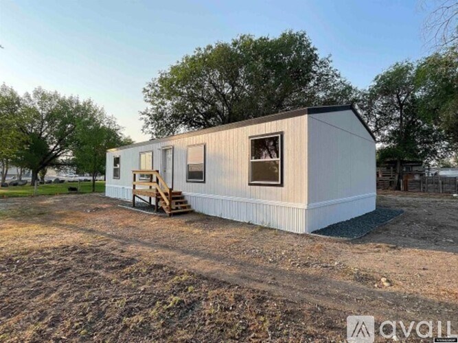 A small white house with a wooden deck and a metal roof is situated in a field.