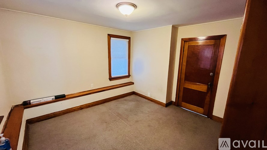 A room with a brown door, a window, and a carpeted floor.
