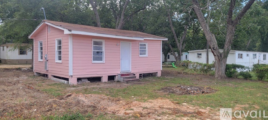 A pink house with a white door is surrounded by trees and other houses.