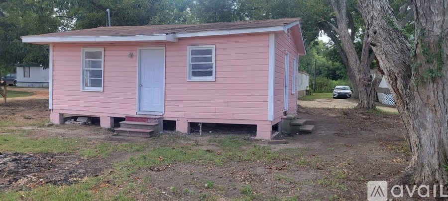 A small pink house with a white door and a tree in front.