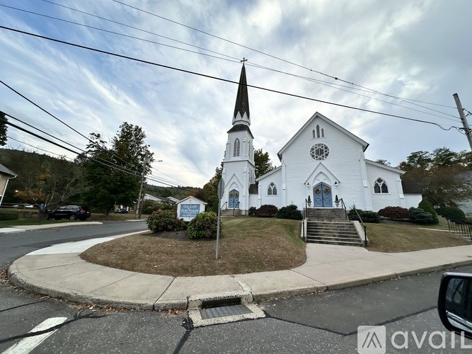 A white church with a steeple and a clock on the front is surrounded by a grassy area and a road.