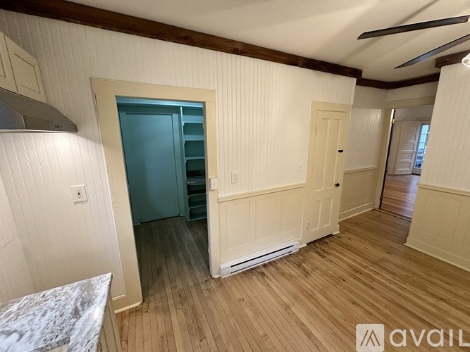 A room with wooden floors and white walls, featuring a kitchen island and a blue door.