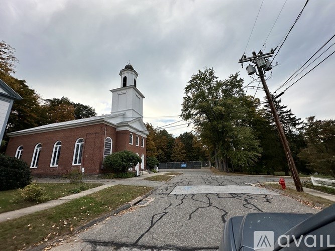 A white church with a steeple and a brick facade is surrounded by trees and a cracked street.