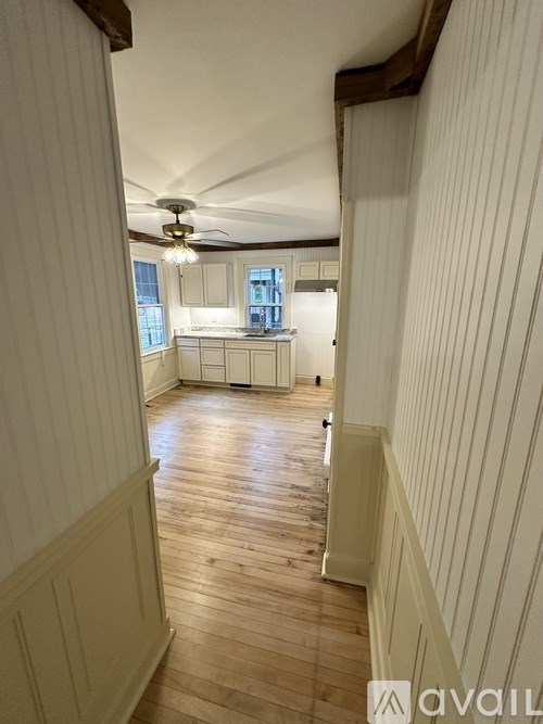 A hallway with wooden floors and white walls leading to a kitchen.