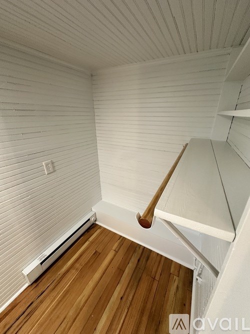 A room with a wooden floor and a white wall with a light switch.