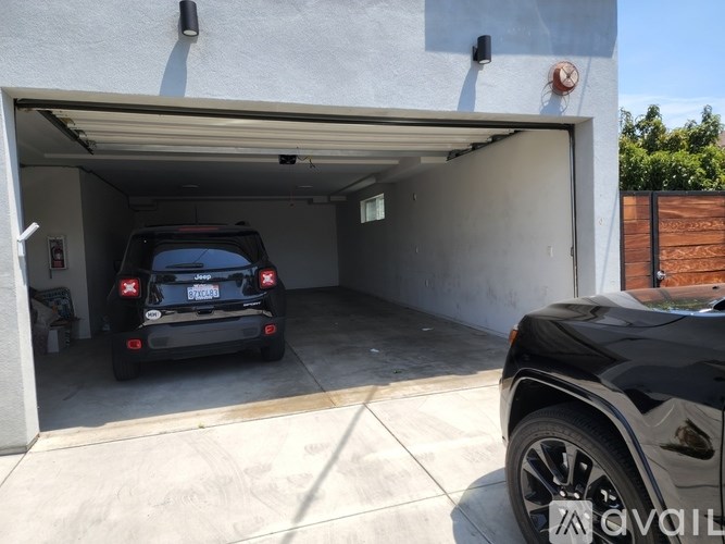 A black car is parked in a garage with a white car inside.