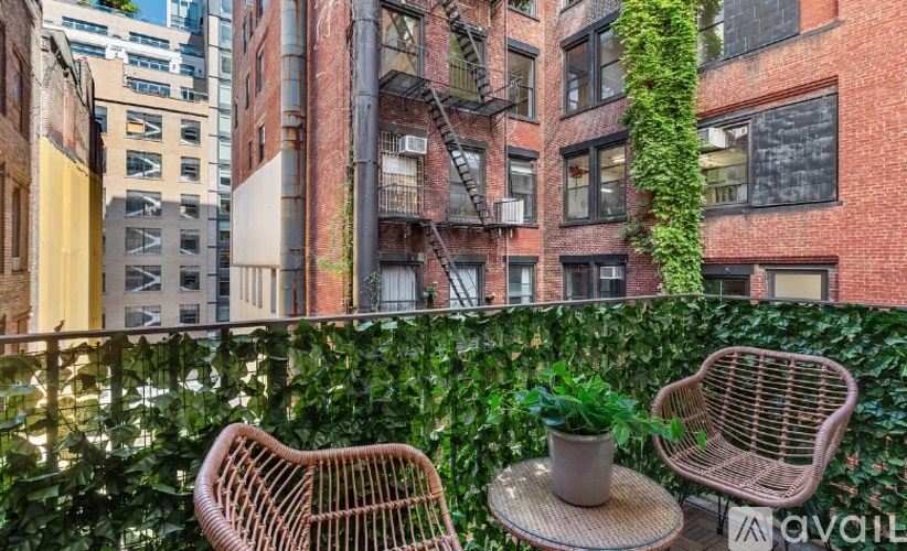 Two chairs and a table are on a balcony with a green plant.