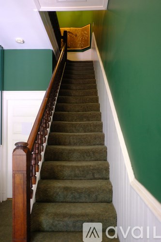 A staircase with a green carpeted runner and wooden balusters.