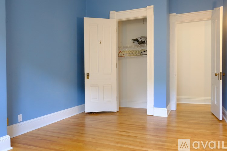 A room with a white door and a white closet with clothes in it.