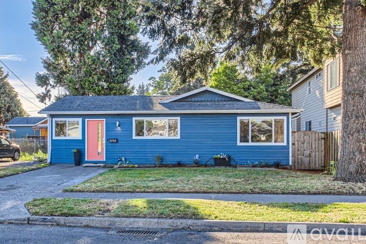 A blue house with a red door is surrounded by greenery.