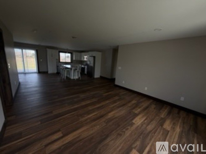 A spacious room with wooden flooring and a dining area in the background.