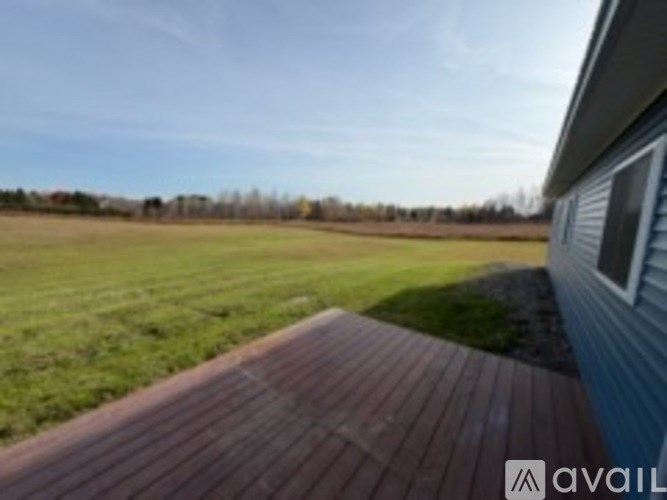 A wooden deck leads to a house with a field in the background.