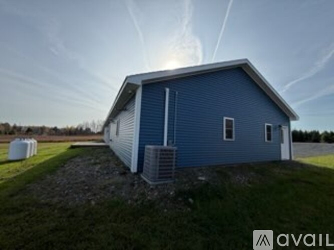 A blue building with a white door and windows is situated on a grassy area with a clear sky above.