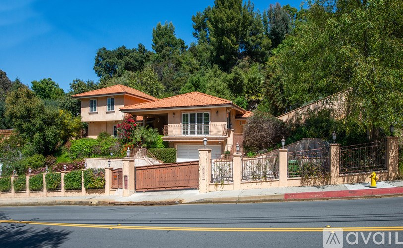 A house with a red roof is surrounded by a fence and trees.