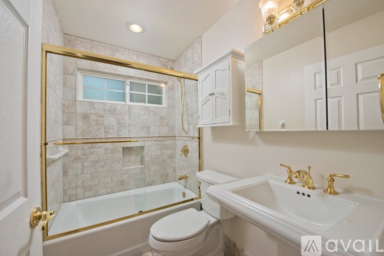 A bathroom with a white toilet, a sink with gold faucets, and a glass shower enclosure with a gold frame.