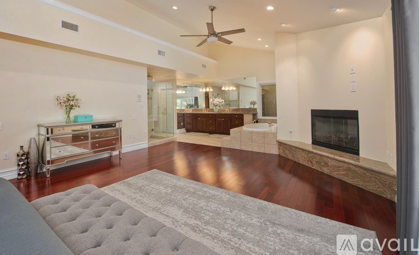 A spacious living room with a grey tufted ottoman in the foreground.