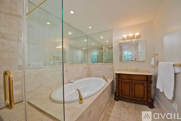 A bathroom with a glass shower door, a bathtub with a gold faucet, a wooden cabinet, and a mirror above the sink.