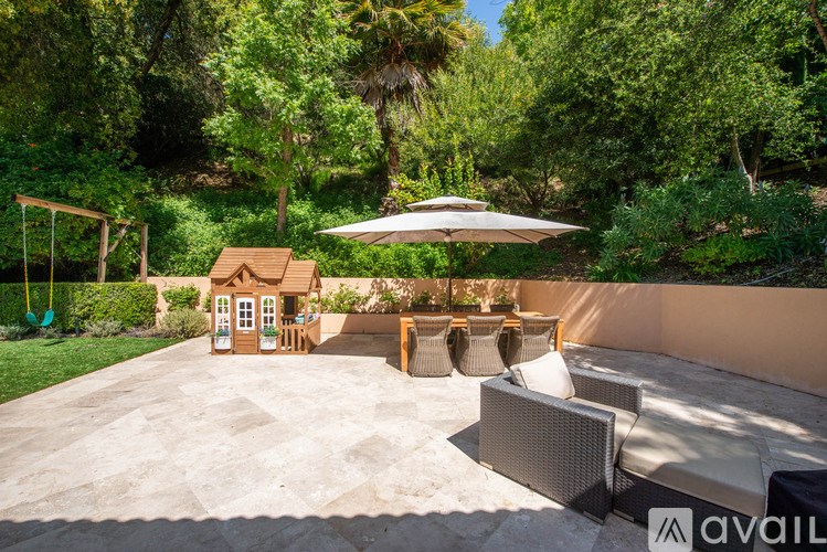 A patio with a white umbrella and a small wooden house.