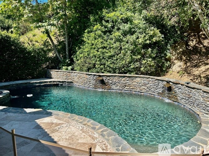 A small pool surrounded by a stone wall and trees.