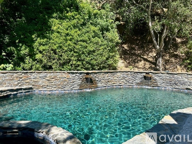 A pool surrounded by a stone wall and trees.