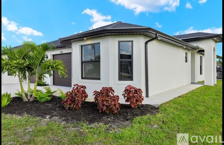 A white house with a black roof and a garden in front.