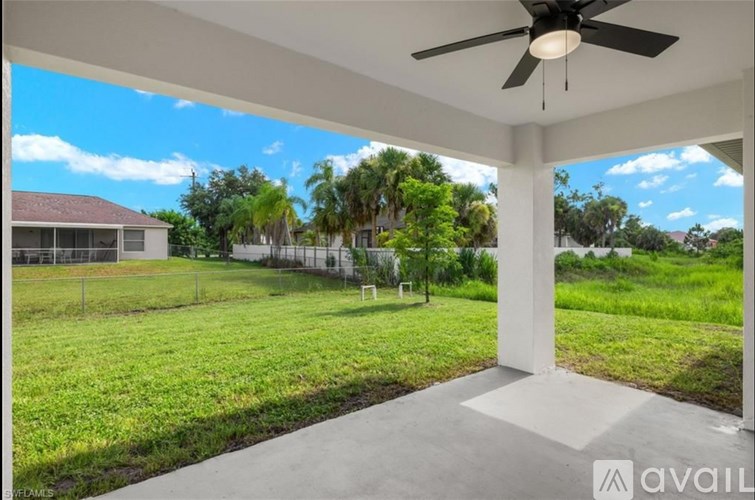 A patio with a ceiling fan and a view of a green lawn and trees.