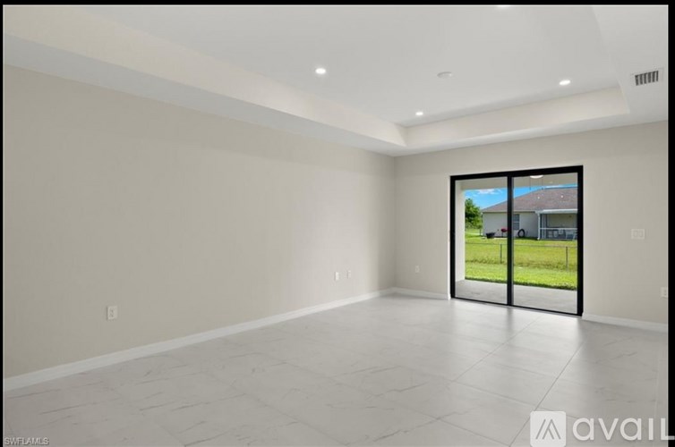 A spacious empty room with a view of a green lawn and a house through the glass door.