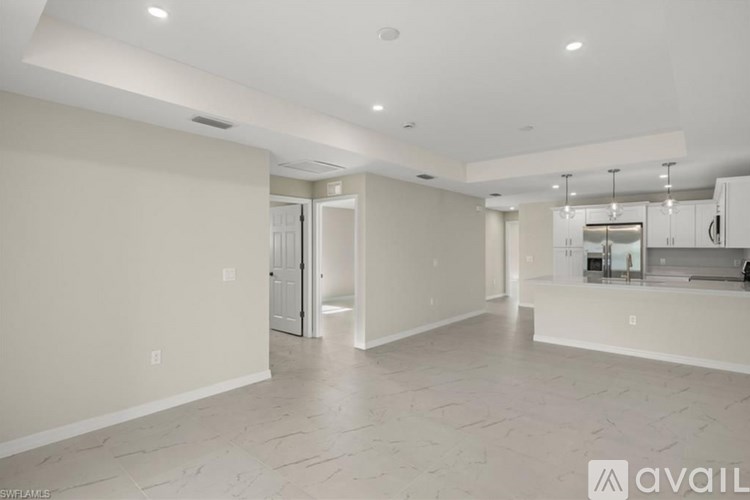 A spacious, empty room with a kitchen area in the background.
