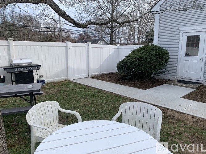 A backyard with a white fence, a grill, and a small table.