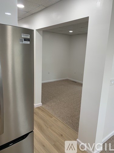A room with a stainless steel refrigerator on the left and a carpeted floor.