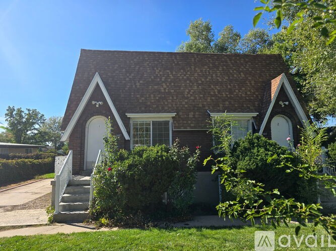 A small house with a brown roof and a white door is surrounded by greenery.
