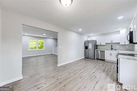 A spacious kitchen and living room with white cabinets and a wooden floor.
