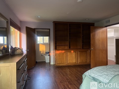 A bedroom with a large bed, wooden cabinet, and a kitchen area with a counter and drawers.