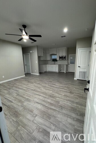 A spacious room with a ceiling fan and a kitchen area in the background.