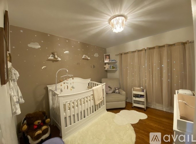 A baby nursery with a white crib, a teddy bear, and a cloud wall decal.