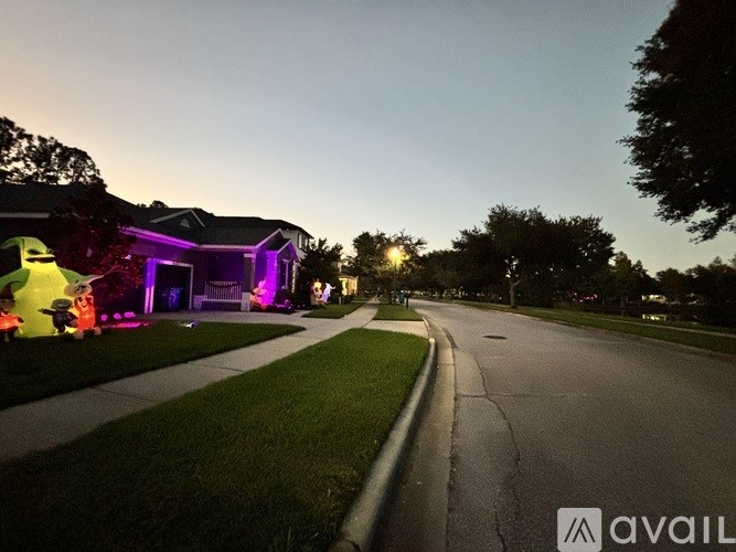 A street view of a residential area with houses on the left and a tree-lined street on the right.